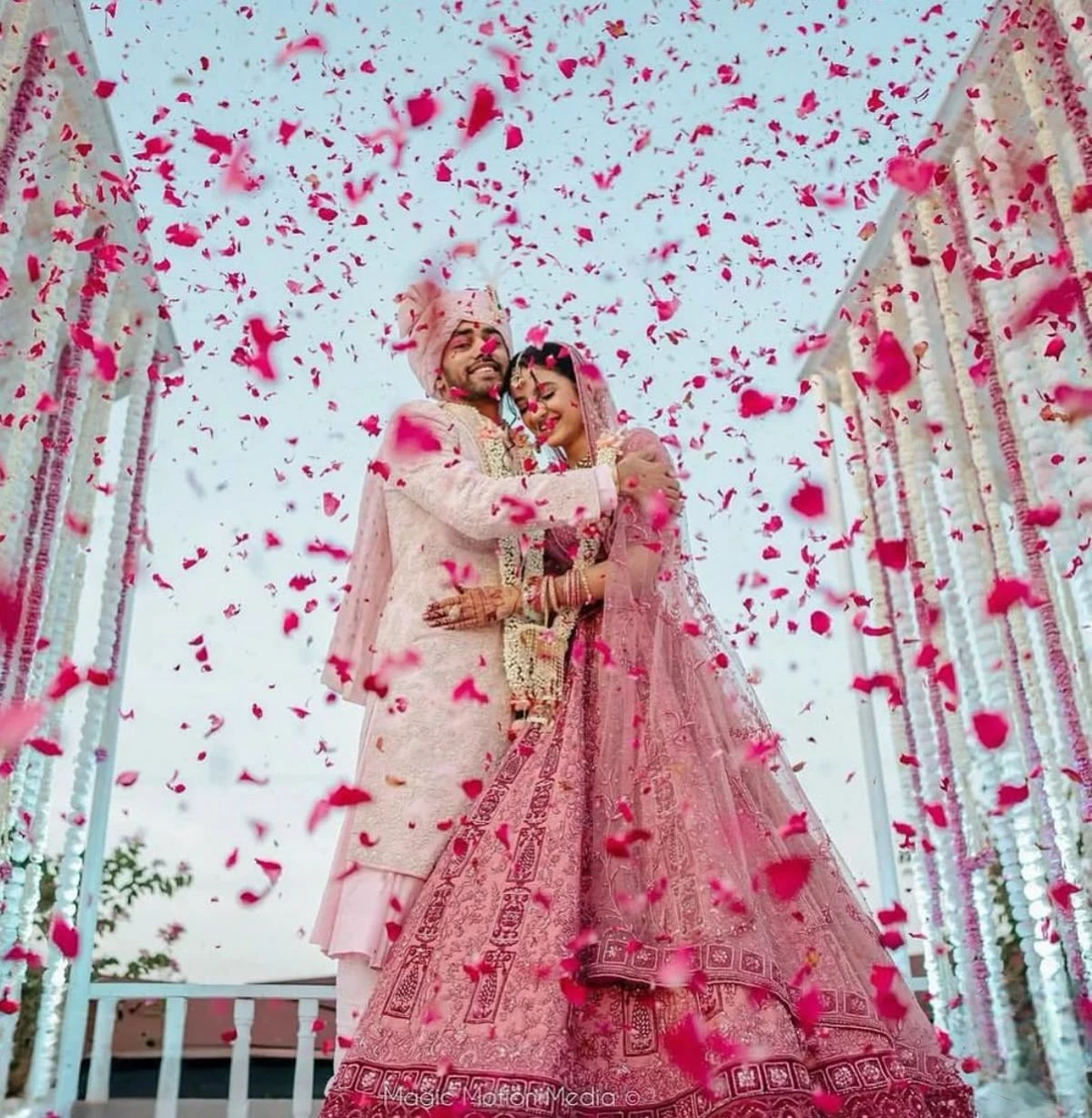 Indian wedding couple standing under a shower of flower petals for dreamy wedding photo